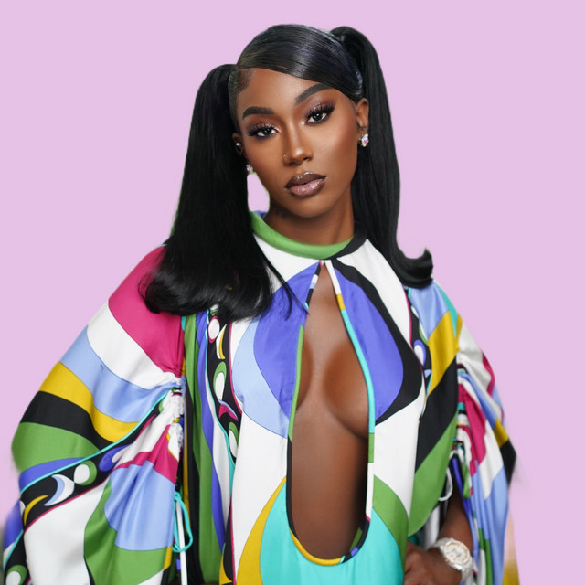 Flo Milli posing in a colorful outfit against a pale pink background